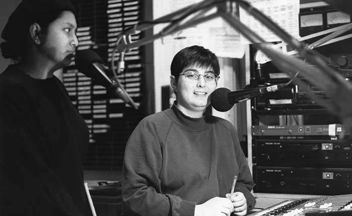 Radio hosts Lorraine Henderson and Christine Lavergne stand in front of their microphones in a radio studio.