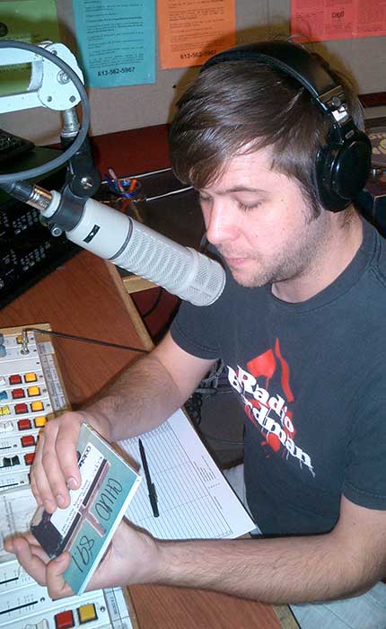 Entrepreneur Luke Martin, at the microphone, in front of a mixing table, in a radio studio.