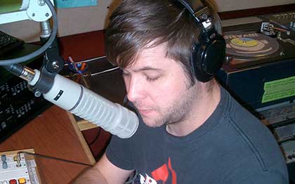 Entrepreneur Luke Martin, at the microphone, in front of a mixing table, in a radio studio.