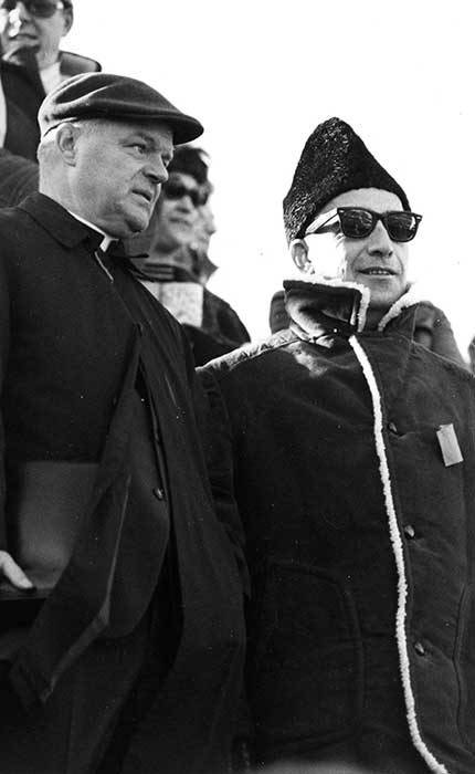 Le père Roger Guindon dans les gradins du stade de football en compagnie du vice-recteur aux ressources, Allan K. Gillmore, en 1970.